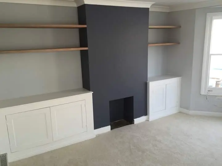 Built-in alcove cupboards with oak shelves beside a navy chimney breast