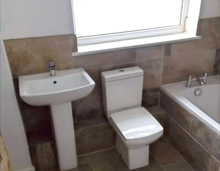 Bathroom with a new basin, toilet and bath against brown stone-effect tiles