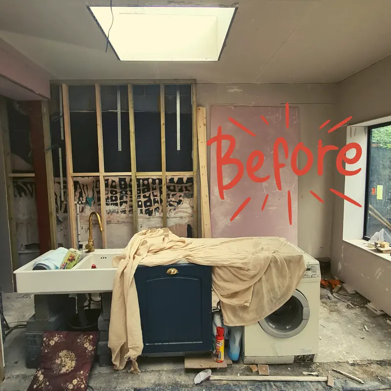 The same room with exposed stud walls and a washing machine before the renovation